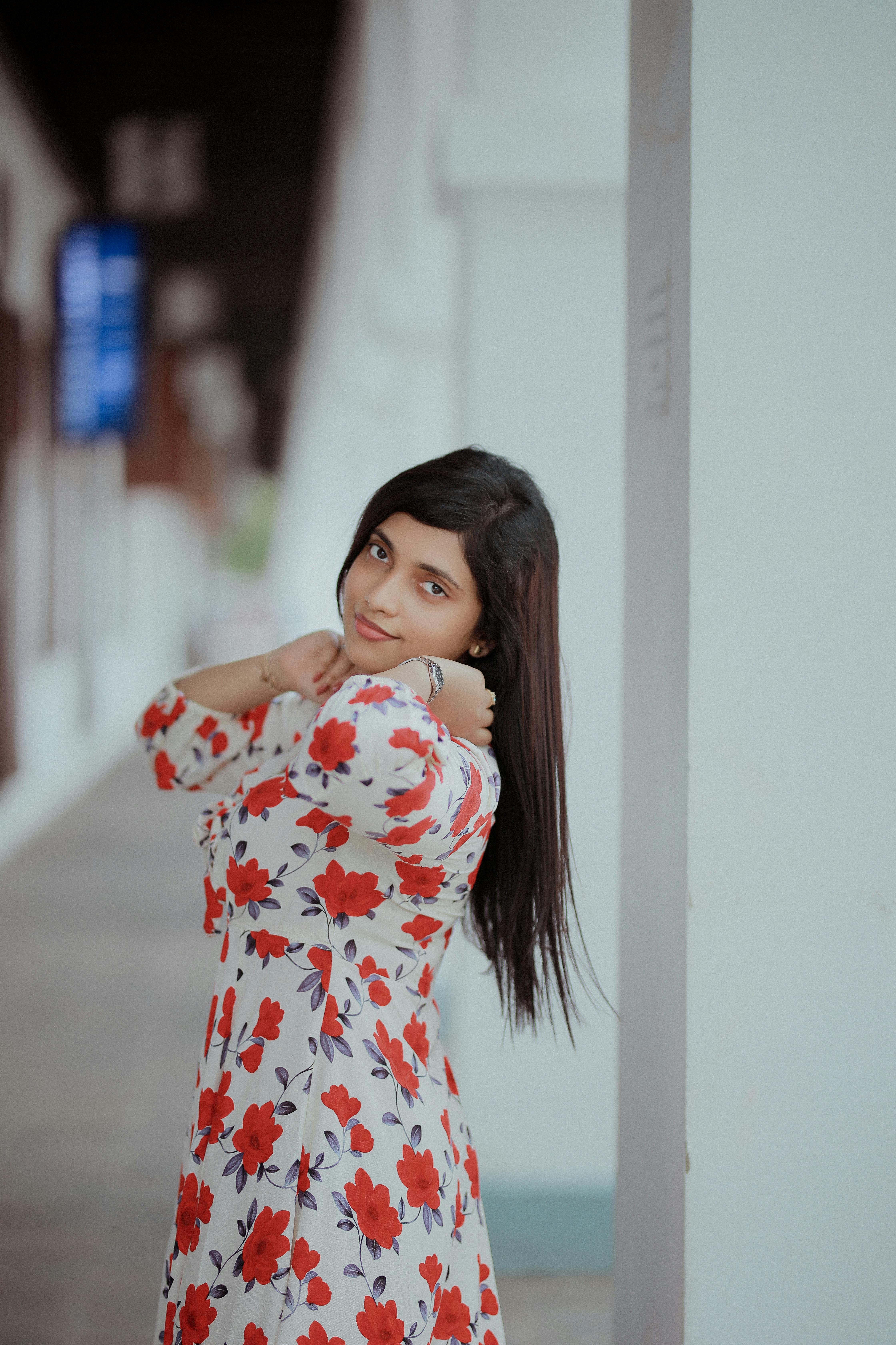 Free A woman in red floral dress adjusts her hair in a stylish outdoor setting. Stock Photo