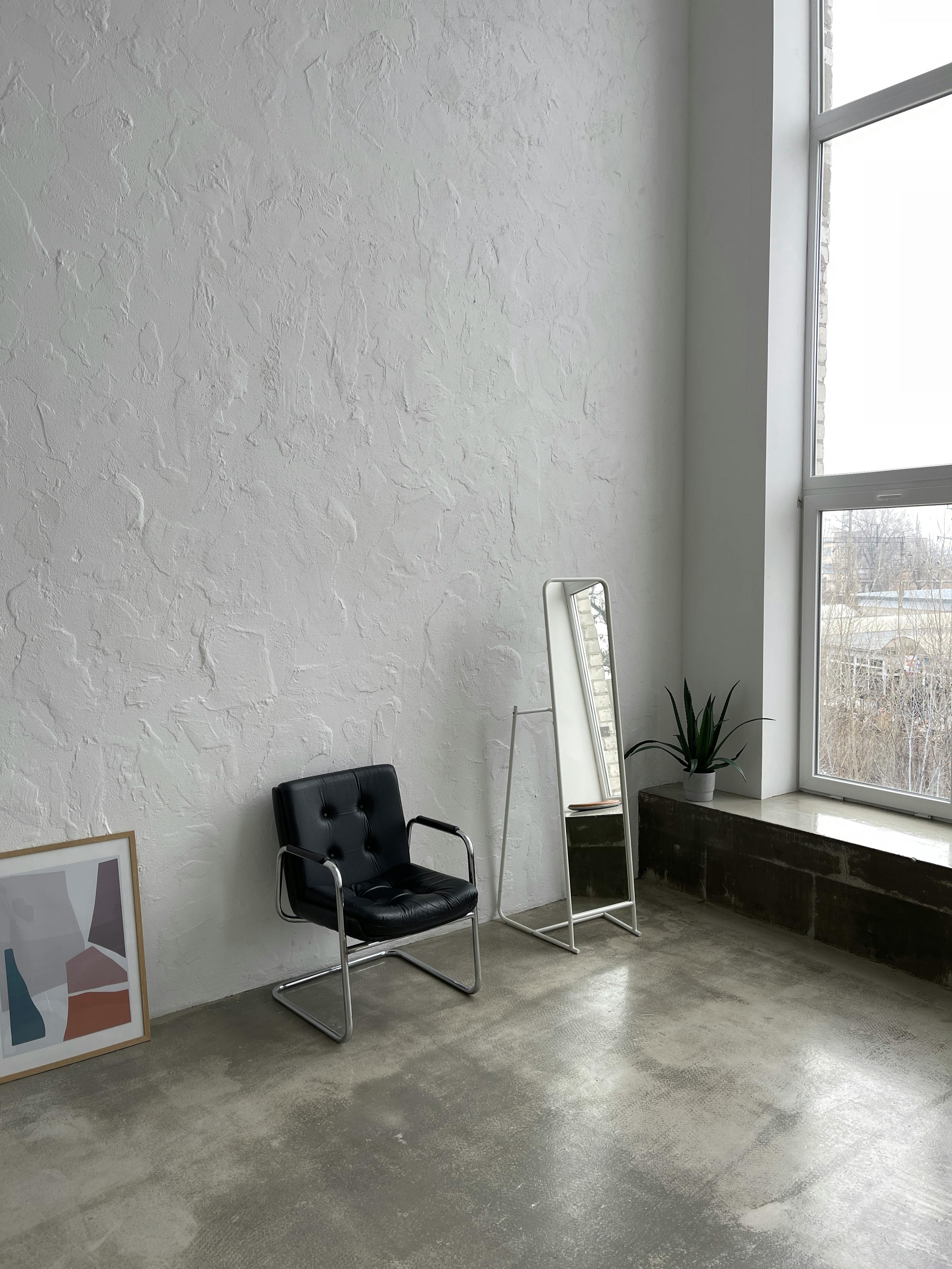 A stylish minimalist room featuring a black armchair, a tall mirror, and a large window.
