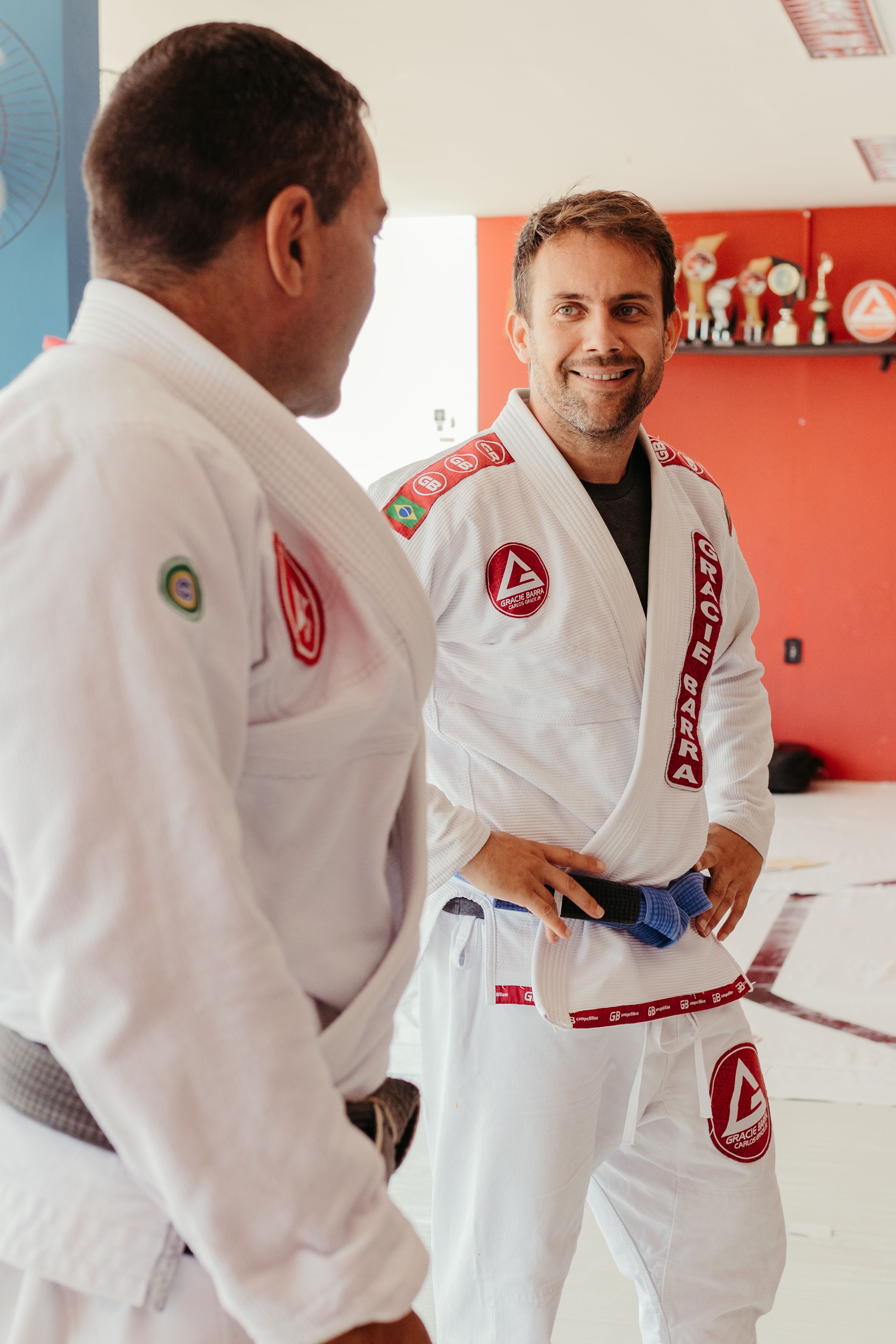 Two men in gis engaging in martial arts training at an indoor gym setting.
