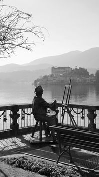 Black and white photo of an artist sculpture by a tranquil lakeside.