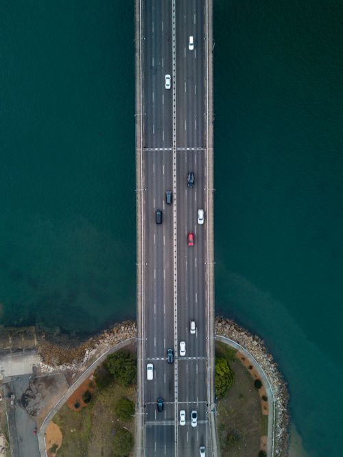 Free Aerial view of vehicles crossing Sydney Harbour Bridge during the day over blue waters. Stock Photo