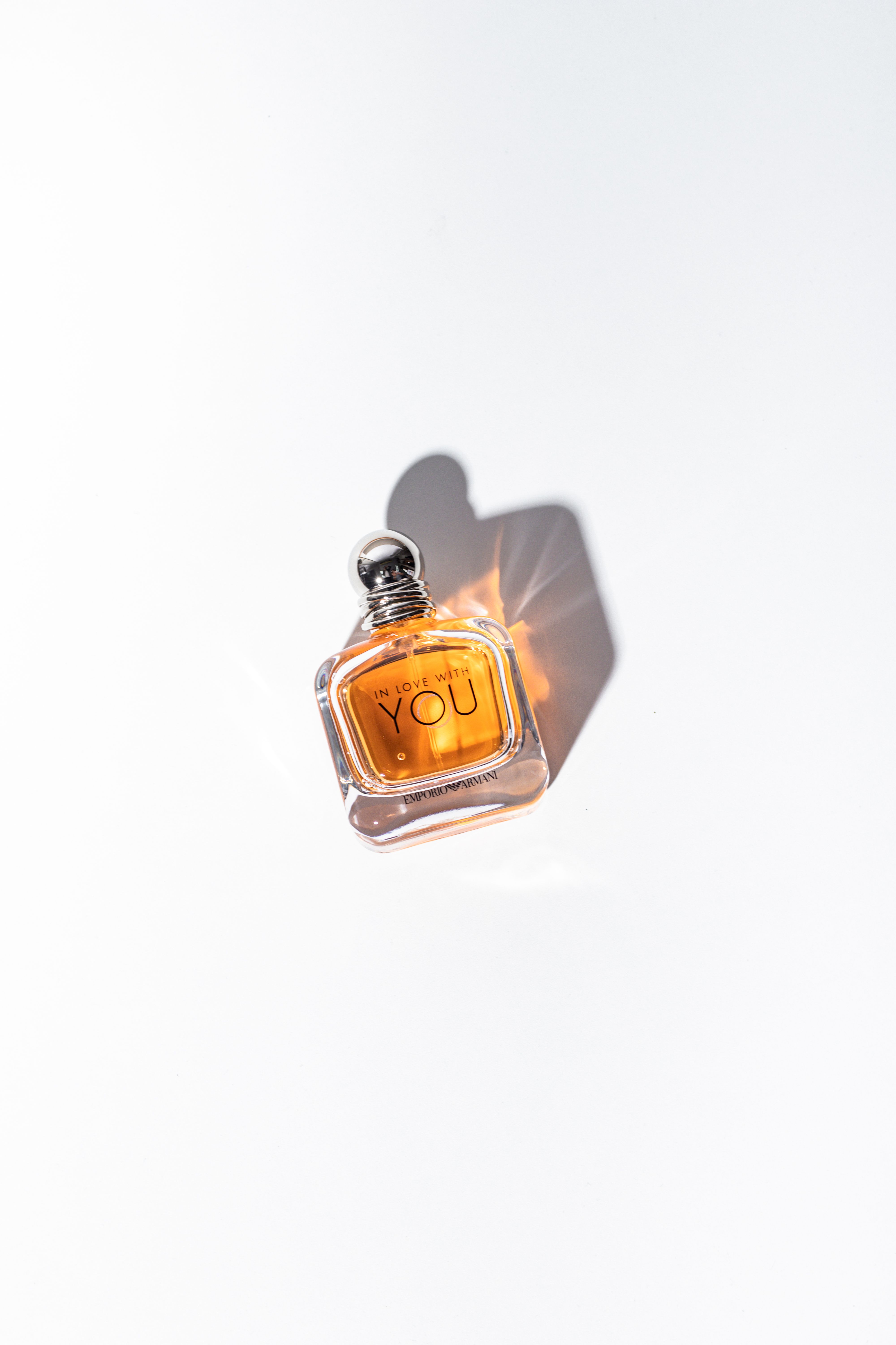 Minimalist photograph of a perfume bottle casting a shadow against a white background.
