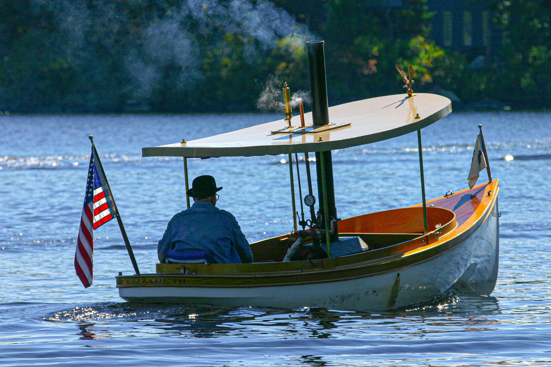 A vintage steamboat cruises leisurely on a serene river, adorned with an American flag.