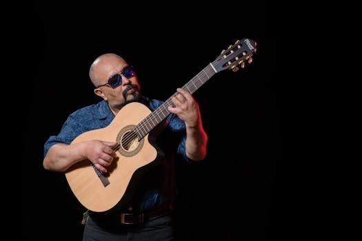A bald musician passionately strumming an acoustic guitar under studio lights.