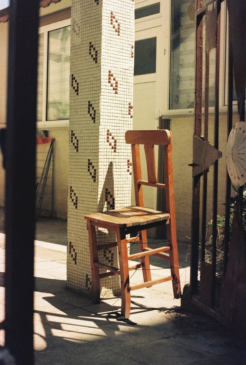Free Weathered wooden chair casting a shadow in an outdoor Turkish courtyard with mosaic tile column. Stock Photo
