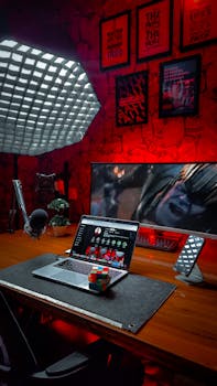 A sleek home office setup featuring a laptop, monitor, and microphone with red lighting for an inspiring workspace.