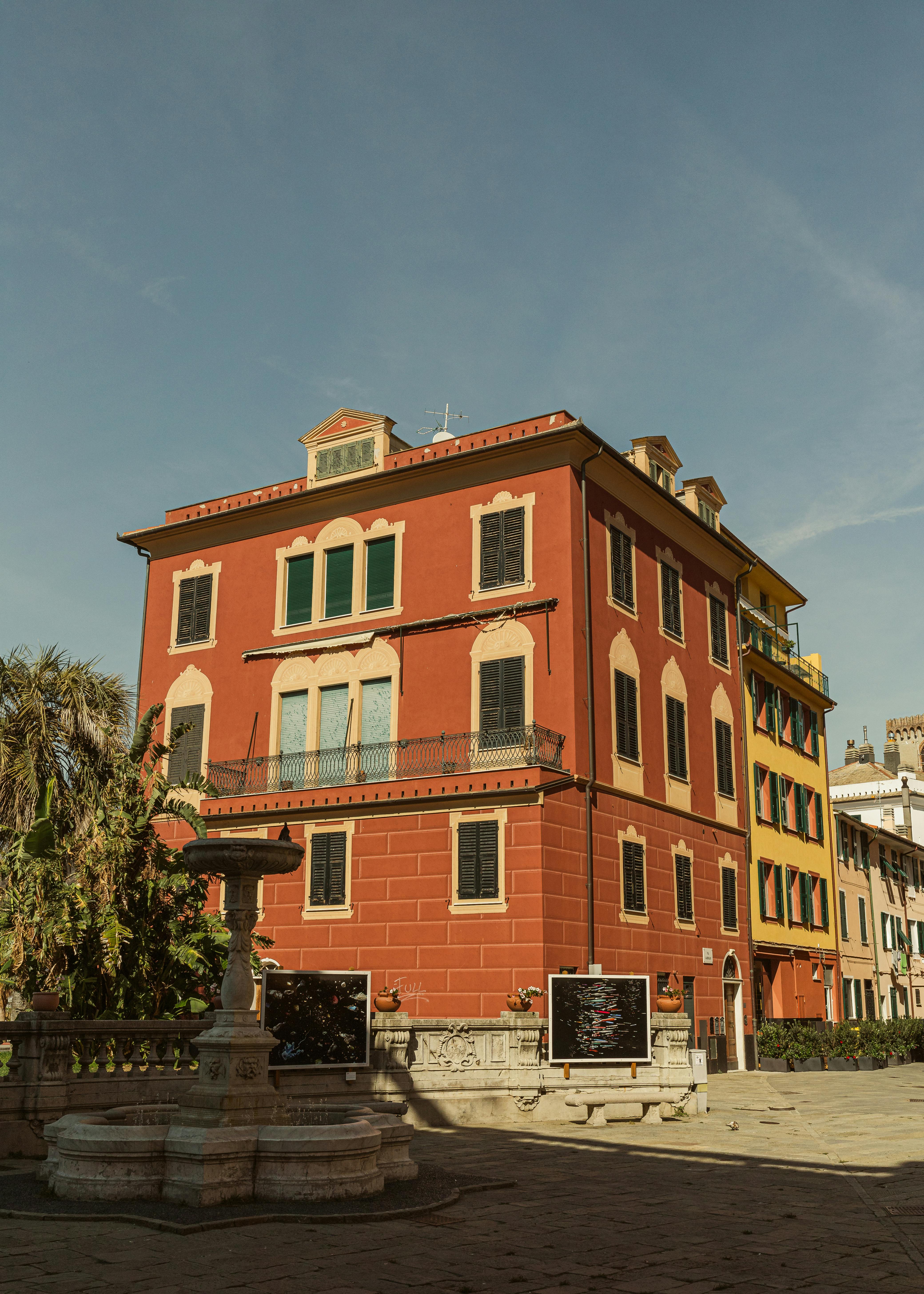 Vibrant three-story building facade with fountain in a sunny urban setting.