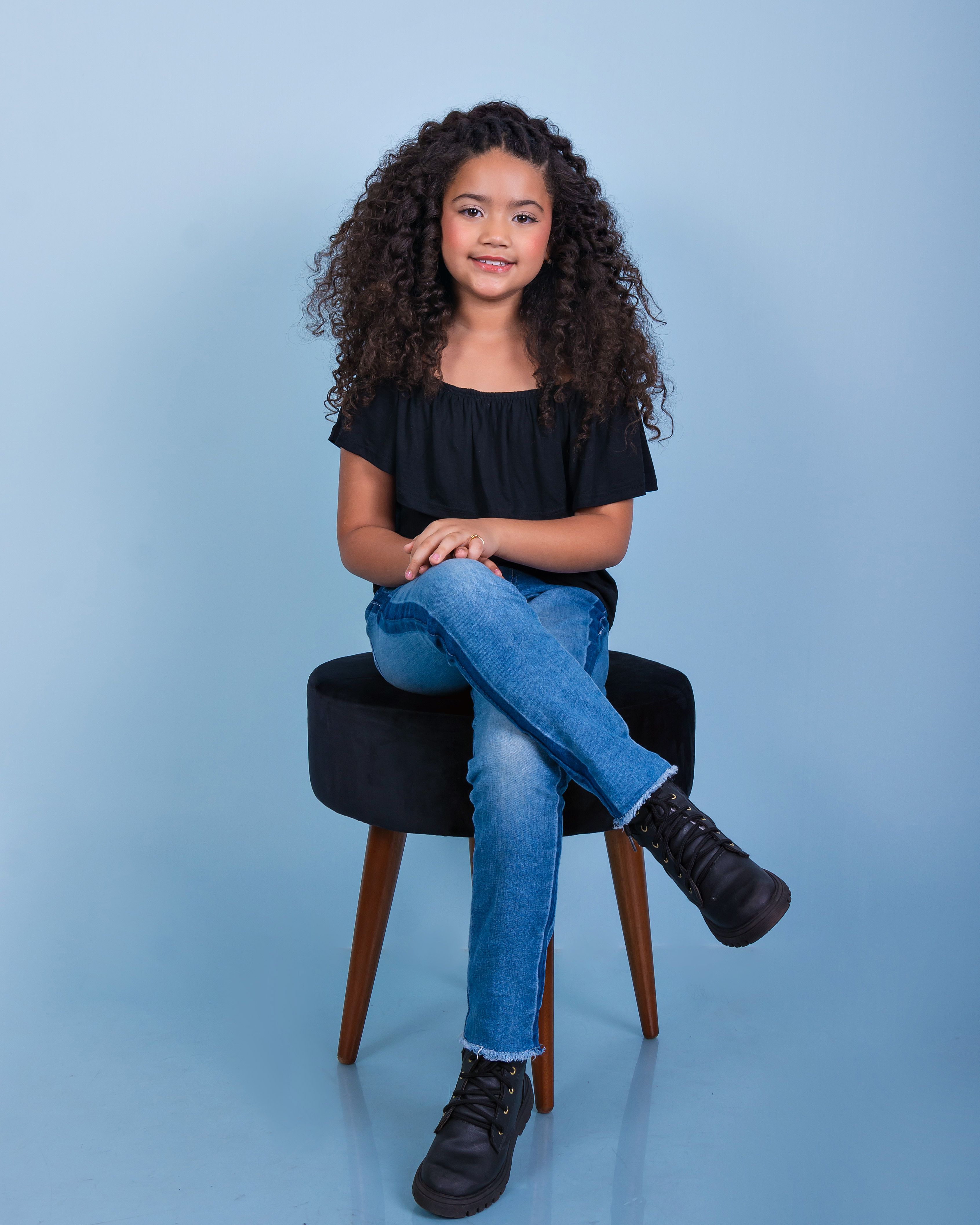 Portrait of a smiling girl in a black blouse and jeans against a blue background.