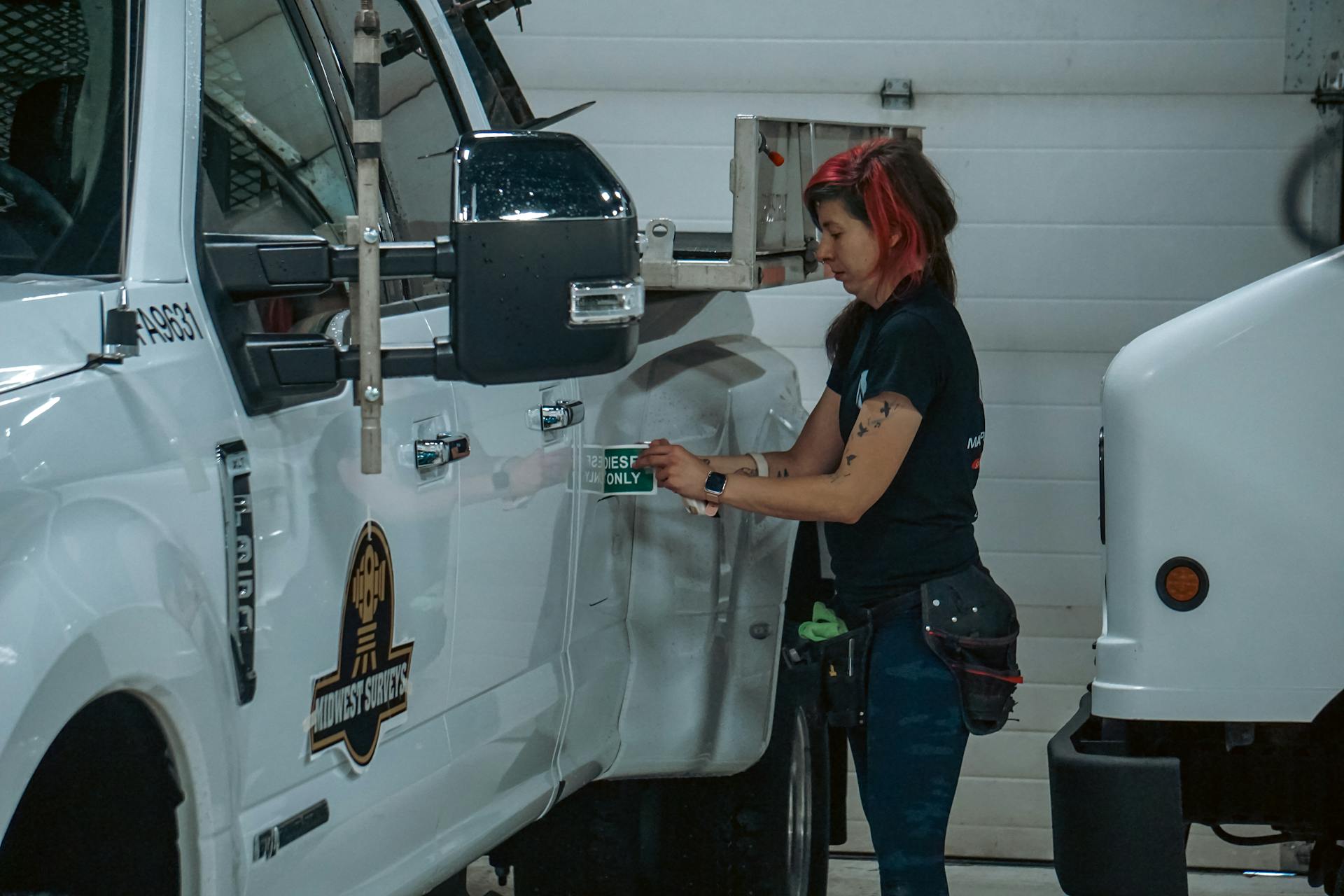 Woman applying a safety sticker on a truck in an indoor garage setting, Calgary, Canada.