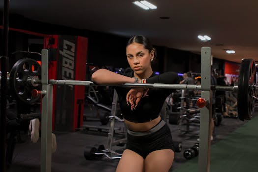 Confident female athlete posing with a barbell in an indoor gym setting.