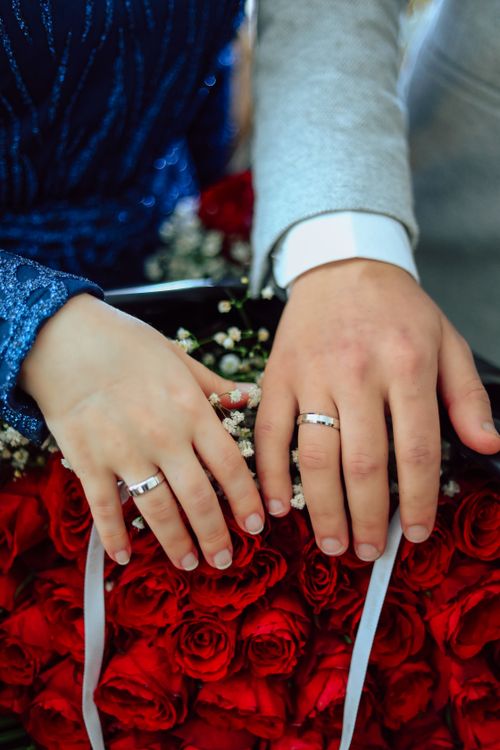 Free Close-up of bride and groom's hands showing wedding rings over a bouquet of red roses. Stock Photo