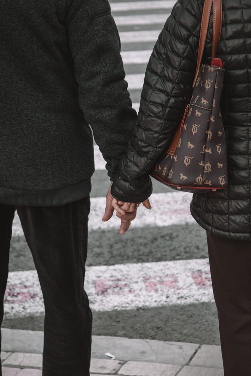 Free A couple in warm attire holding hands at a street crosswalk in Valencia, Spain, showcasing companionship. Stock Photo
