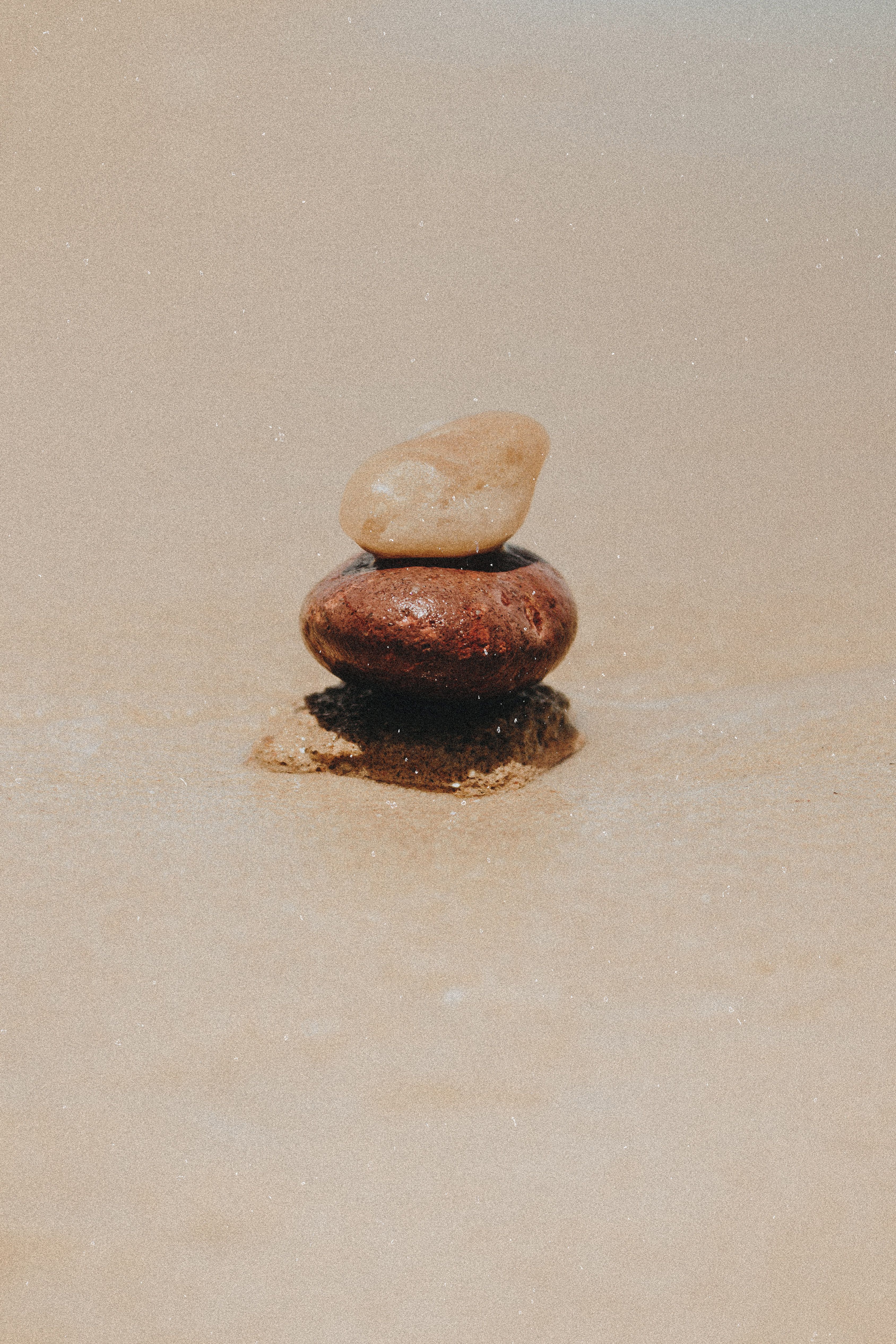 Two smooth stones balanced on sand