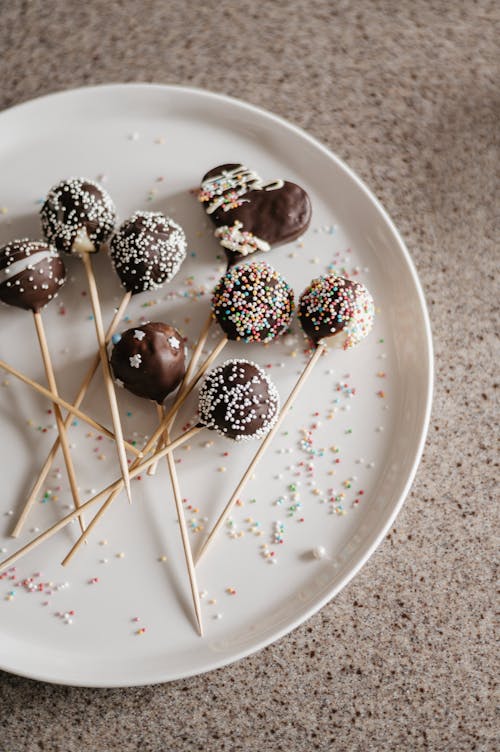Cake Pops with Chocolate and Sprinkles Lying on a White Plate 