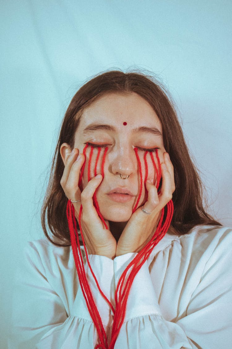 Conceptual Photograph Of A Woman With Red Strings Attached To Her Face 