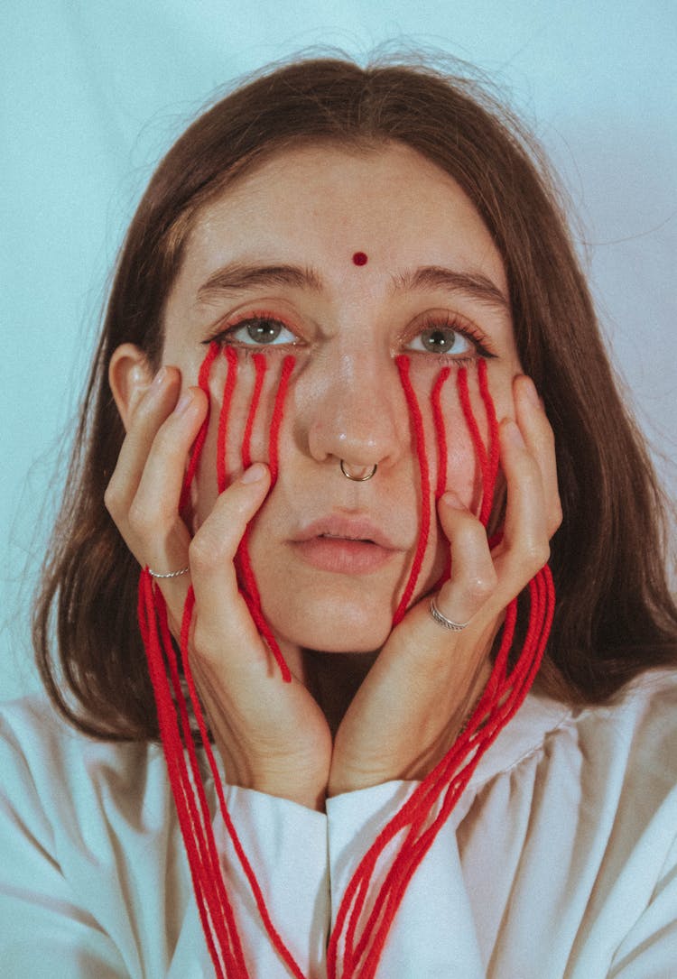 Conceptual Photograph Of A Woman With Red Strings Attached To Her Face 