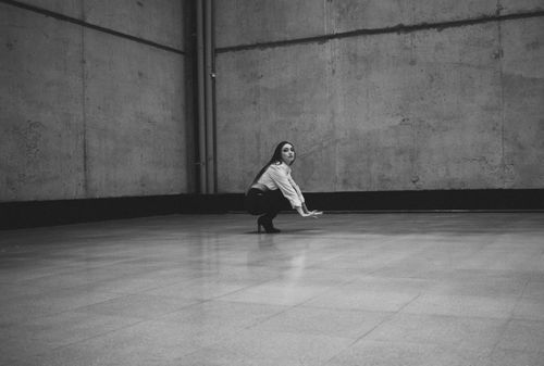 Free A woman crouches in a stylish pose against a textured urban wall. Stock Photo