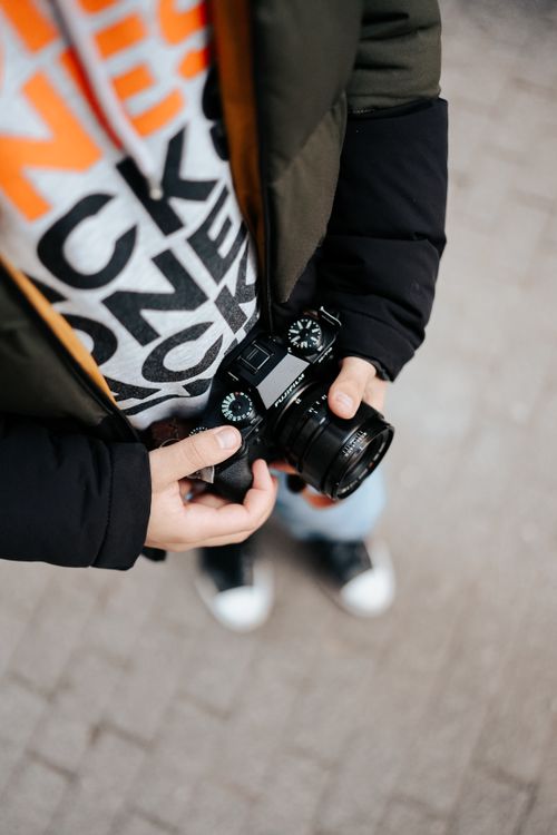 Free Person holding camera in casual attire, ready for street photography. Stock Photo
