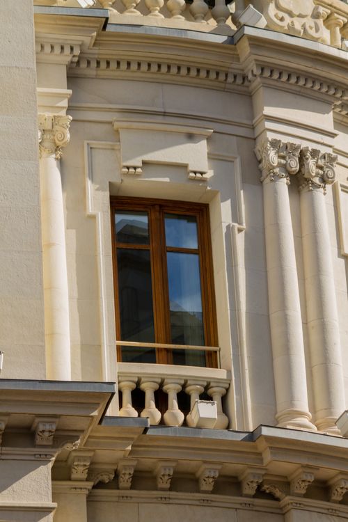 Free Close-up of a neoclassical building facade featuring ornate columns and a single wooden window. Stock Photo