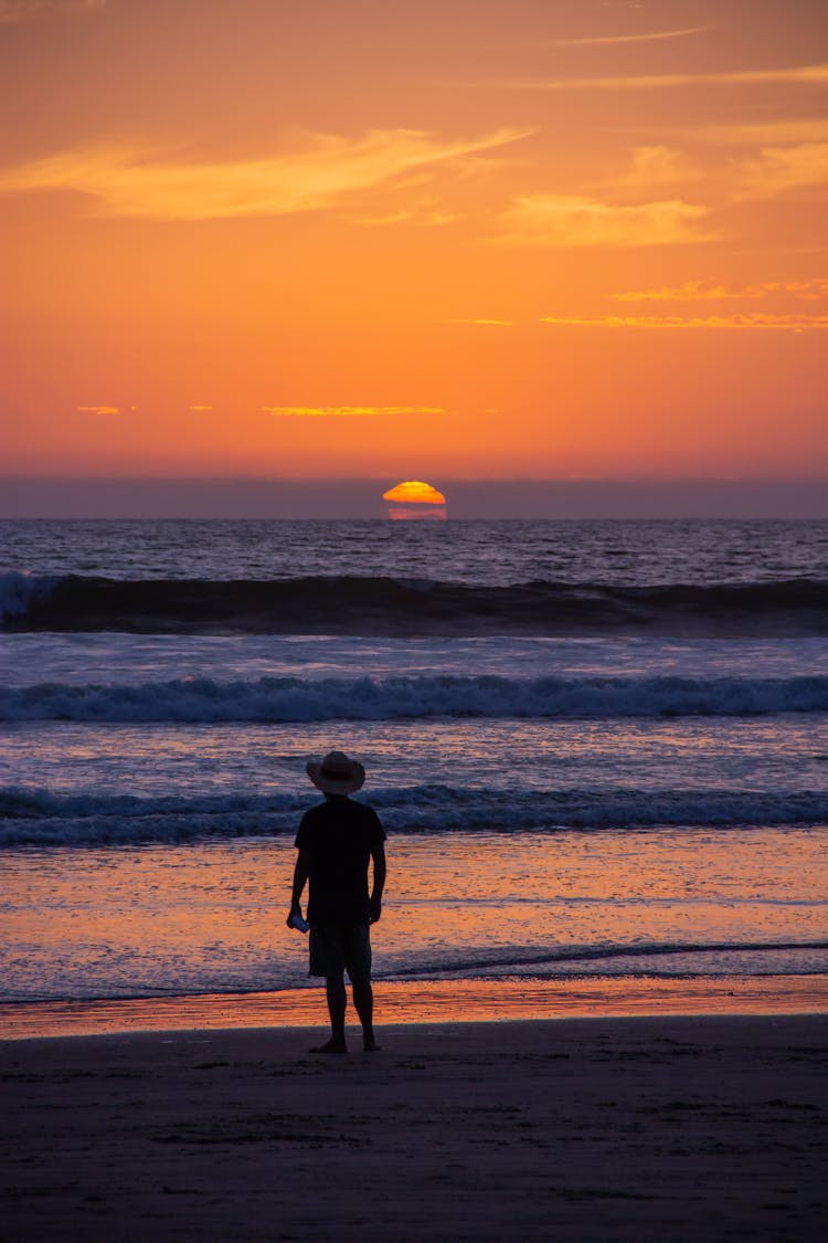 Silhouette Of A Man Standing On A Beach At Sunset 