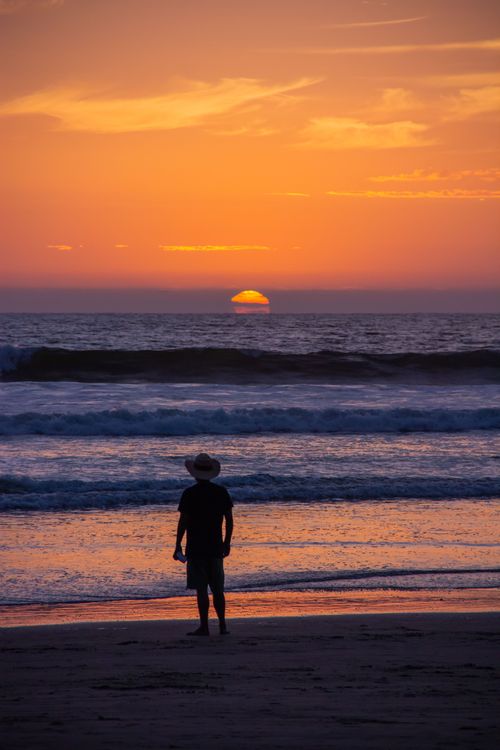 Free A man stands silhouetted against a vibrant sunset on Ensenada beach in Mexico, capturing tranquil beauty. Stock Photo