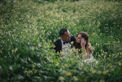 Bride and Groom Sitting on a Green Field 