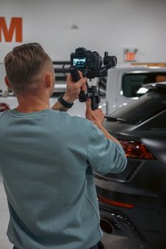 A man records high-end cars indoors using a camera stabilizer in a garage setting.