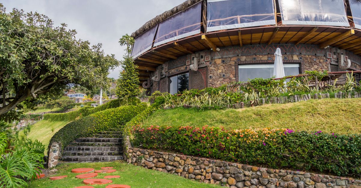 Beautiful stone house surrounded by vibrant garden and stone pathway under a cloudy sky.
