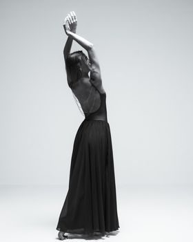 An elegant woman posing in a backless dress, arms raised gracefully in a minimalist studio setting.