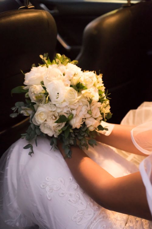 Free A bride sits in a car holding a stunning white floral bouquet, captured elegantly. Stock Photo