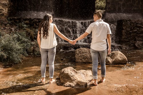 Young Couple Standing near a Waterfall and Holding Hands 