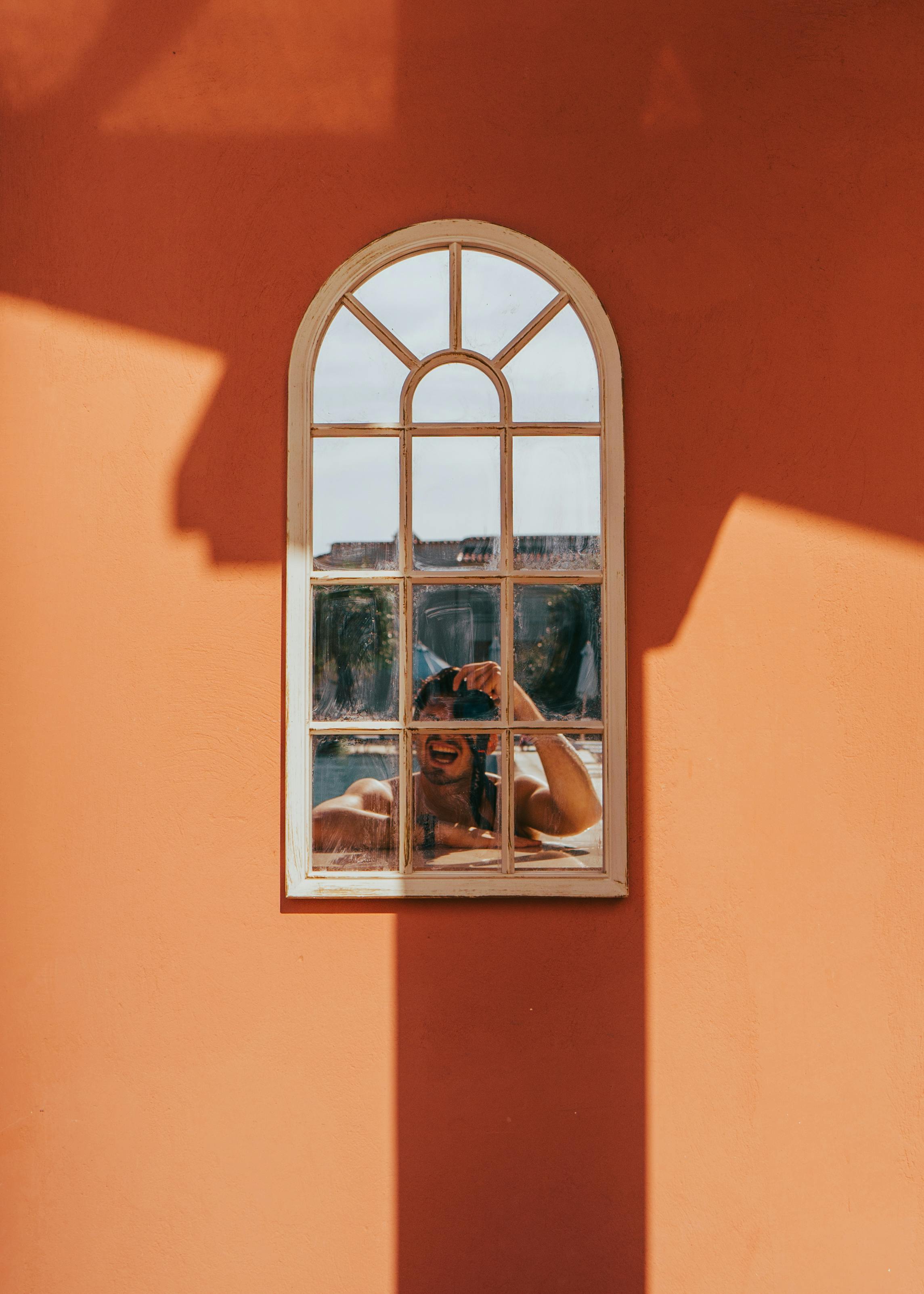 A person reflected in a window on a vibrant orange wall in Corfu, Greece.