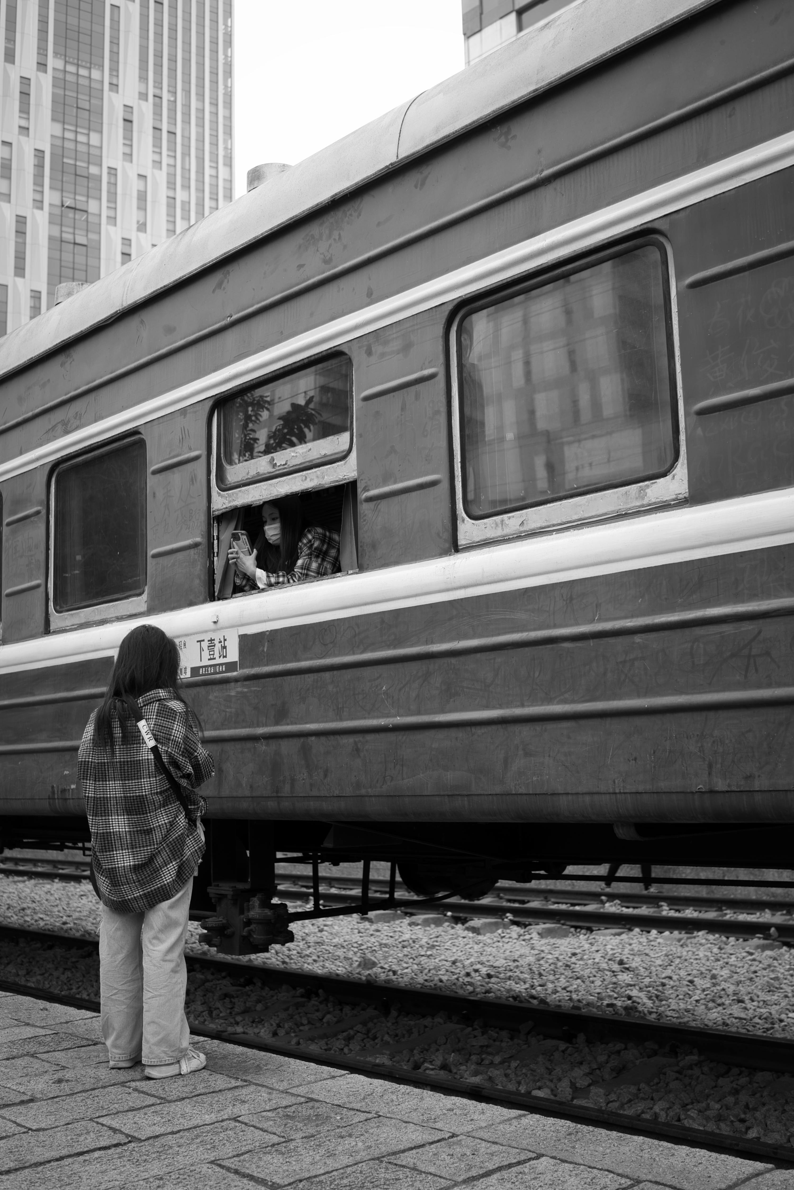A woman in plaid shirt bids farewell to passengers on a departing train.