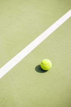 Tennis ball casting shadow on a sunlit green court's white line