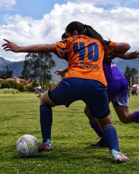 Two women competing for the soccer ball in an intense outdoor match with vibrant jerseys.
