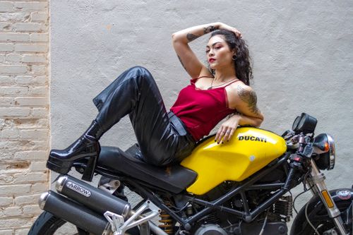 Free Woman in red top and leather pants posing stylishly on a yellow Ducati motorcycle. Stock Photo