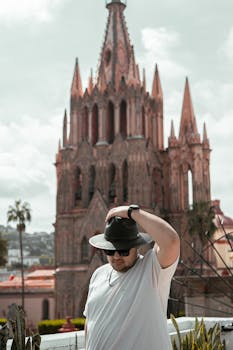 A man in a stylish hat poses in front of the iconic San Miguel de Allende Cathedral in Mexico.