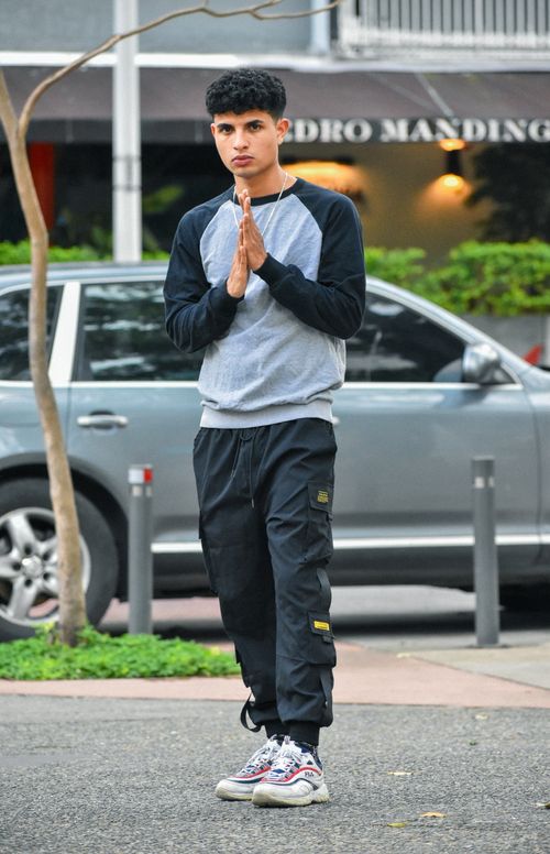 Free Stylish young man in streetwear poses outdoors with a car as background. Stock Photo