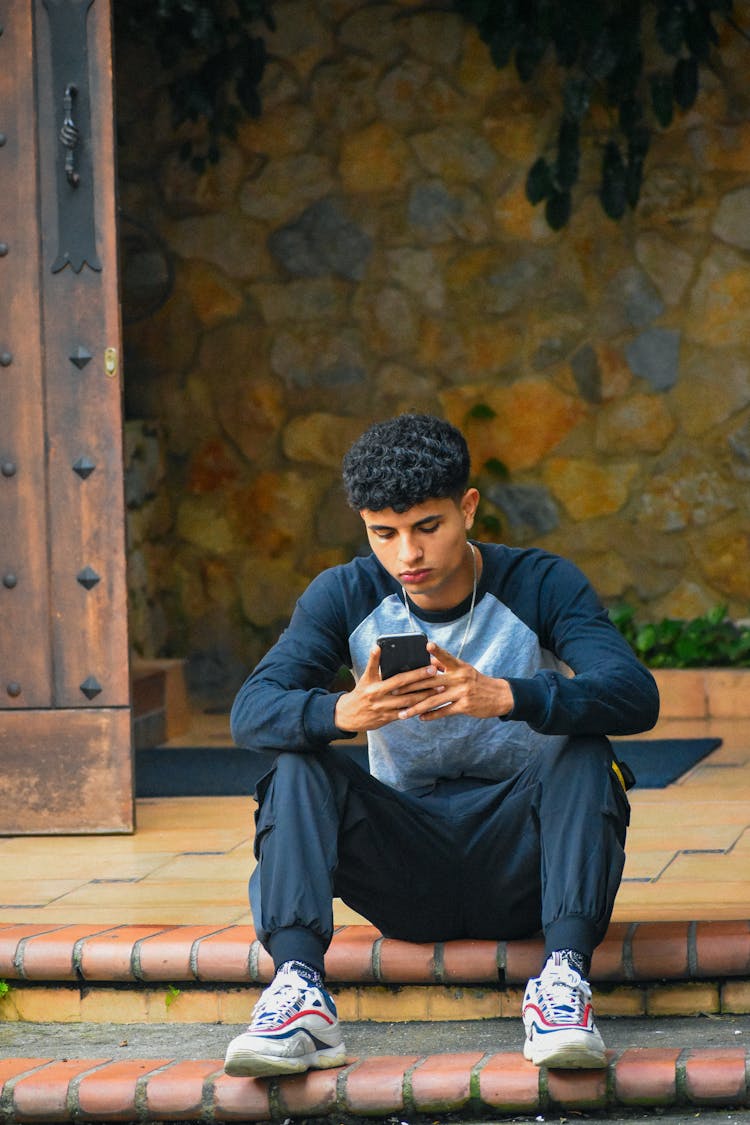 Man In Sweatshirt With Smartphone Sitting On Step