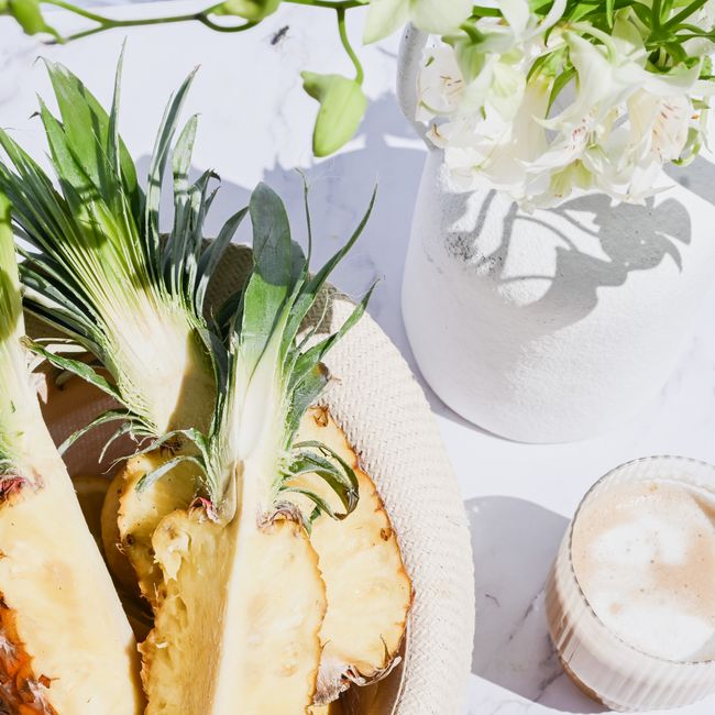 Bright and fresh table setting with sliced pineapples, white flowers, and a coffee on marble.