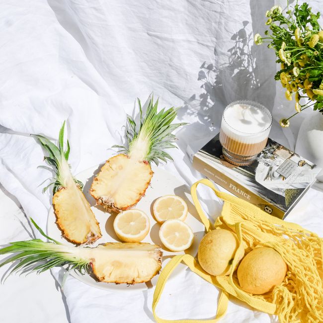 A vibrant flat lay of cut pineapples, lemons, and books set on a white sheet in the sunlight.