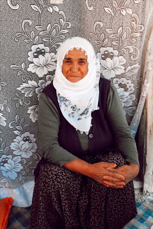 Free Portrait of an elderly woman wearing a floral headscarf, seated against a floral tapestry backdrop. Stock Photo