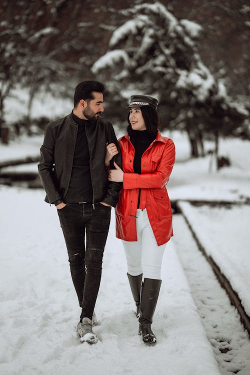 Woman Holding onto a Mans Arm while Walking in a Snowy Park 