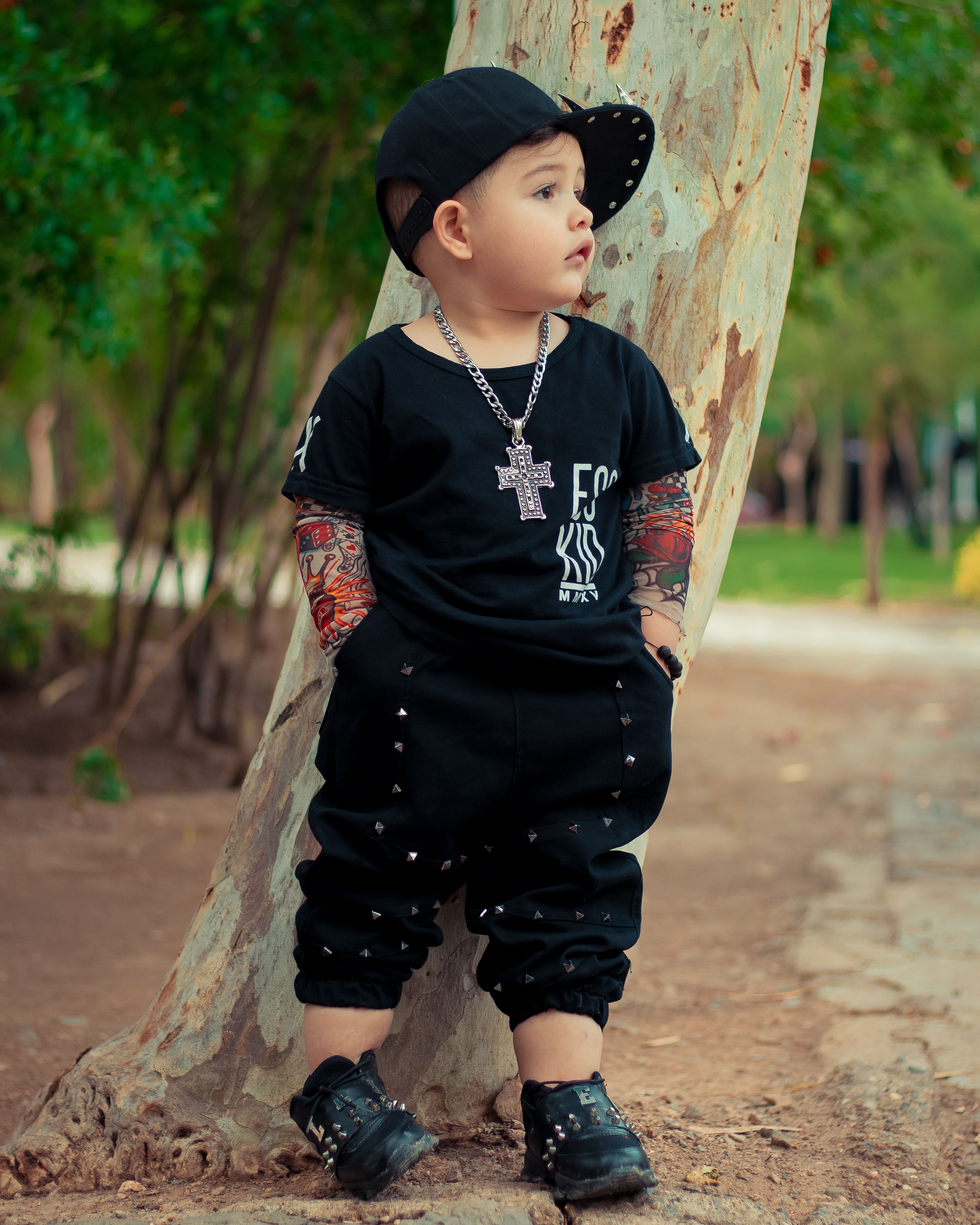 Adorável menino pequeno vestindo um traje estiloso e boné, posando em um parque em Qom, Irã.
