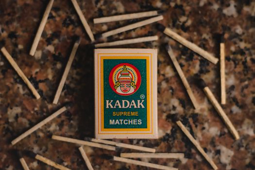Top-down view of a Kadak Supreme matchbox amidst scattered matchsticks on a textured stone surface.