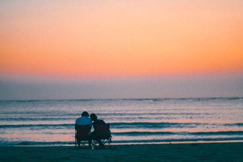 Free A couple sits in chairs on the beach, watching a beautiful sunset over the ocean. Stock Photo