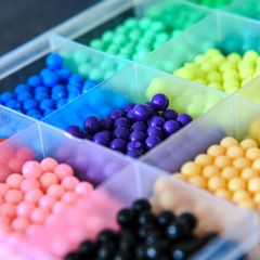 Clear compartment box of bright rainbow beads in pink, purple, blue, green, yellow and black