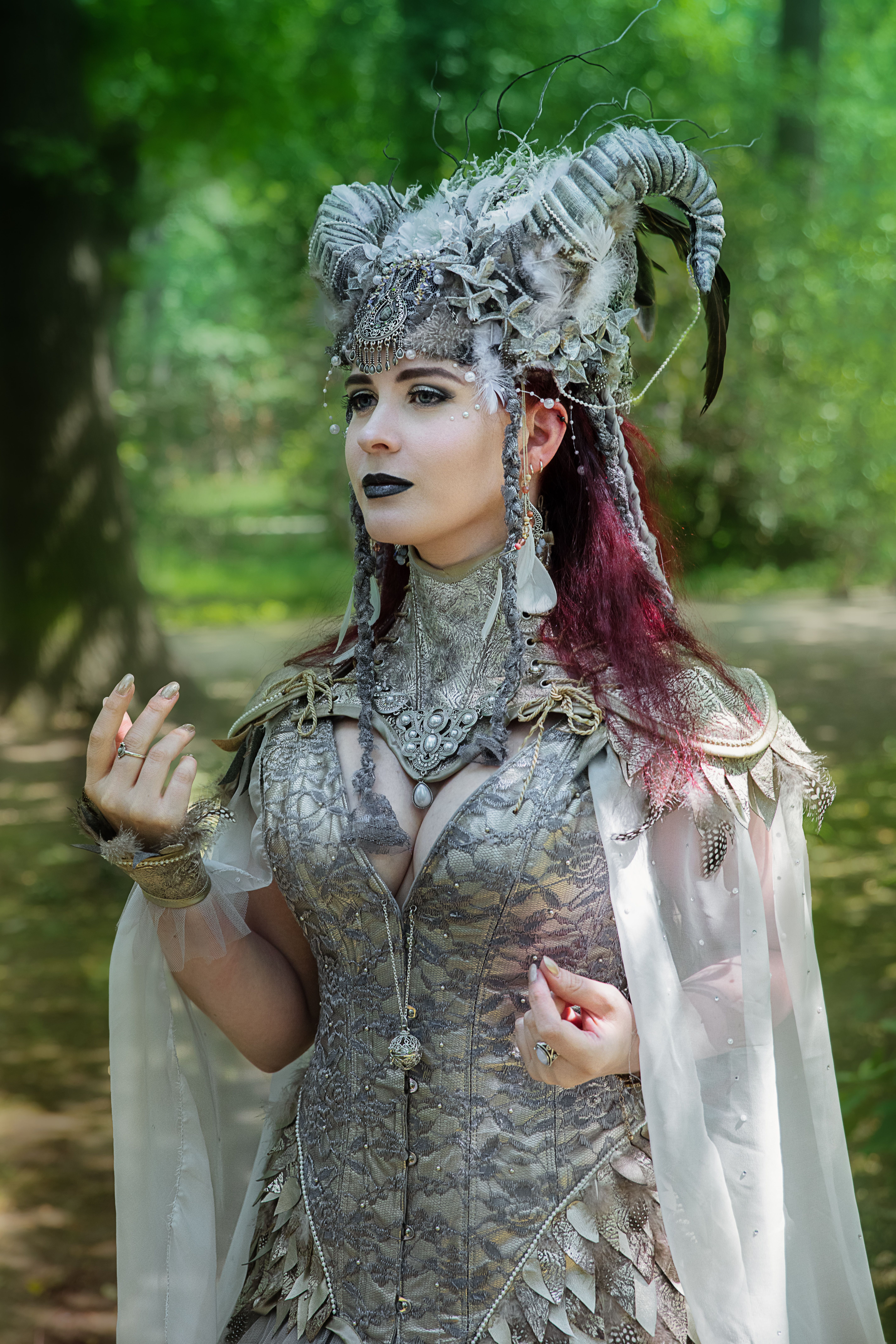 A mystical portrait of a woman in a fantasy costume and elaborate makeup in a forest setting.