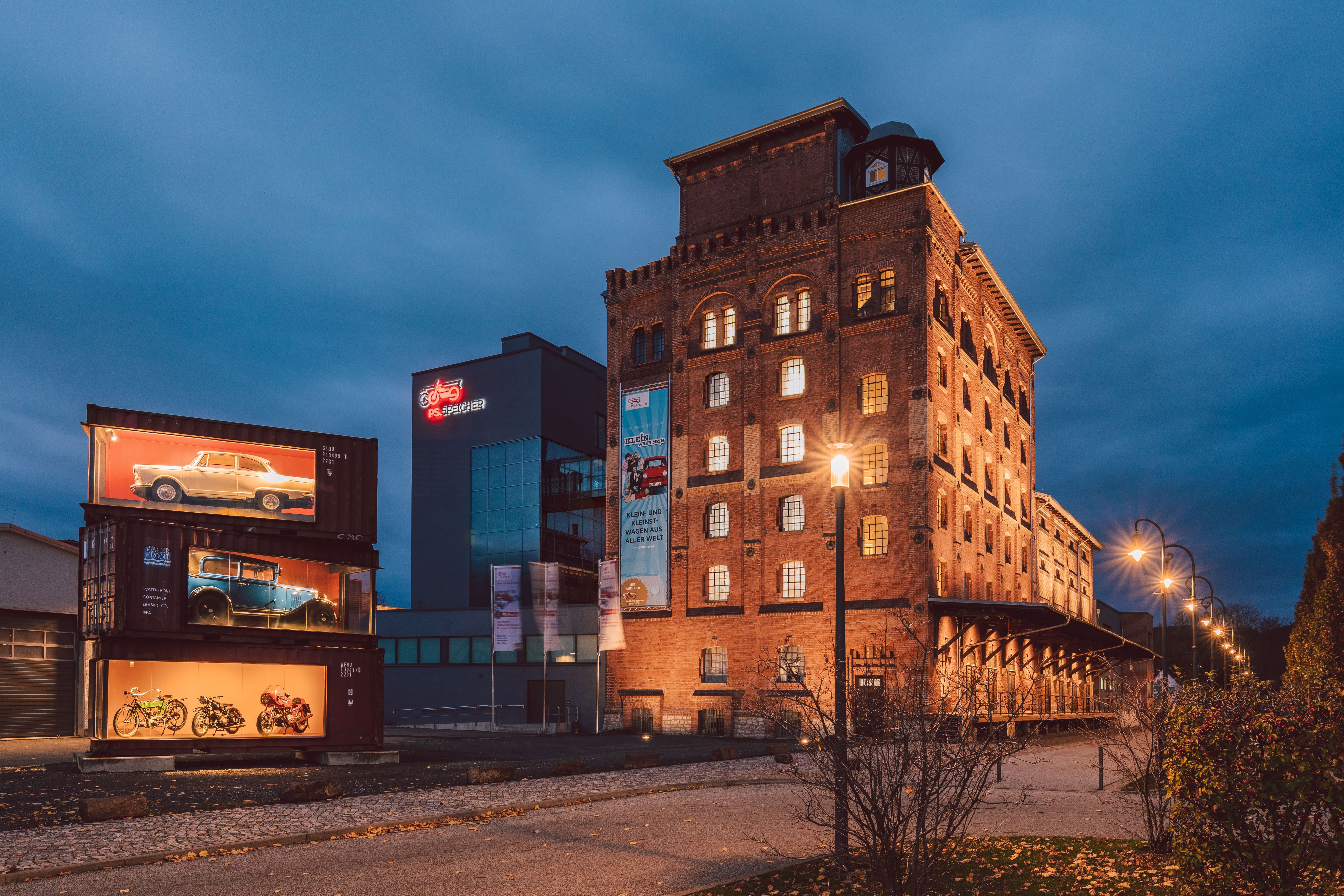 Illuminated PS Speicher Museum in Einbeck, Germany, showcasing vintage vehicles at twilight.
