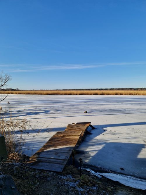 Free A breathtaking winter view featuring a frozen lake and a wooden pier under a clear blue sky. Stock Photo